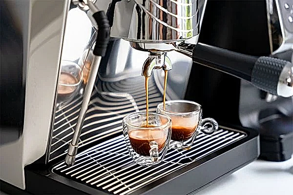 2 Espressotassen stehen in einer Kaffeemaschine und werden von ihr befüllt